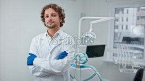 Video Dentist wearing a scrub and standing and smiling in a dental cabinet, in front of a window - Starpik