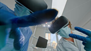 Video Low angle view of two dentists wearing protective masks, gloves and Virtual Reality headsets gesturing under bright procedural lights - Starpik