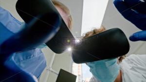 Video Low angle view of two dentists wearing protective masks, gloves and Virtual Reality headsets gesturing under bright procedural lights - Starpik