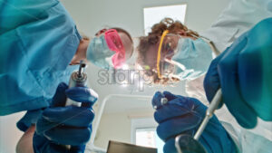 Video Low angle view of two dentists wearing protective masks, goggles, and gloves, holding dental instruments under bright procedural lights - Starpik