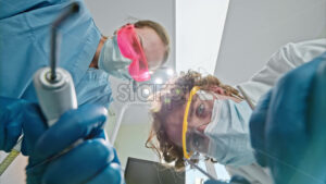 Video Low angle view of two dentists wearing protective masks, goggles, and gloves, holding dental instruments under bright procedural lights - Starpik