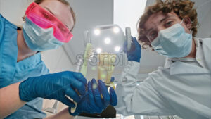 Video Low angle view of two dentists wearing protective masks, goggles, and gloves, showing a big tooth and brush figurine under bright procedural lights - Starpik