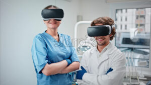 Video  Two dentists wearing scrubs and Virtual Reality headsets while standing and smiling in a dental cabinet, in front of a window - Starpik