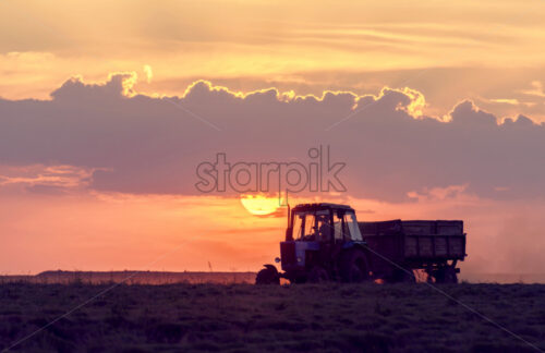 Agricultural machines work in the field, against the background of big red sun at sunset in Moldova - Starpik