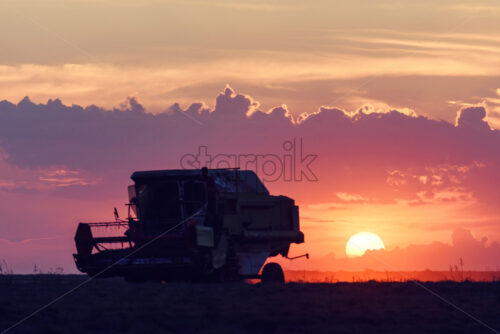 Agricultural machines work in the field, against the background of big red sun at sunset in Moldova - Starpik