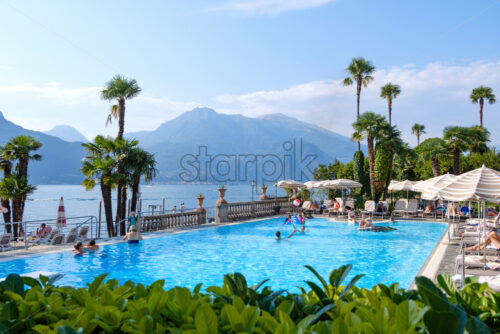 BELLAGIO, ITALY – JULY 31, 2018: People having fun in pool. Kids playing with ball. Mountains and Lake Como on background. Grand Hotel Villa Serbelloni - Starpik