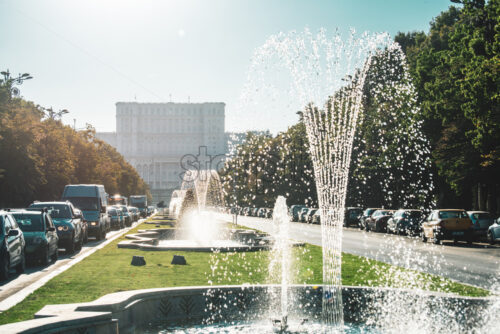 BUCHAREST, ROMANIA – AUGUST 21, 2019: Working fountains on Union Boulevard in sunlight. The Palace of Parliament in background - Starpik