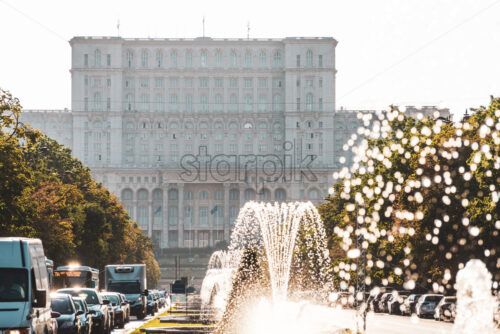 BUCHAREST, ROMANIA – AUGUST 21, 2019: Working fountains on Union Boulevard in sunlight. The Palace of Parliament in background - Starpik