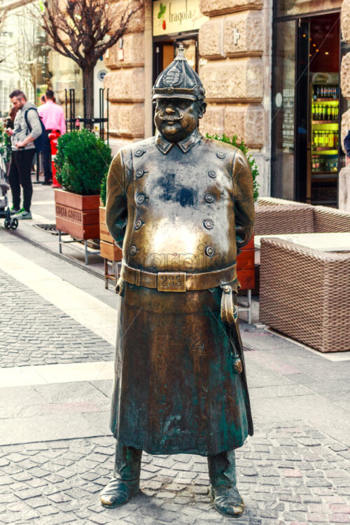 BUDAPEST, HUNGARY – APRIL 10, 2018: The Fat Policeman Statue on Zrinyi street. Tourists and local stores on background - Starpik