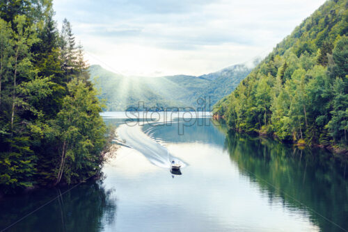 Boat riding on Vidraru Lake at sunset. Green mountains on sides. Traces behind. Fagaras, Romania - Starpik