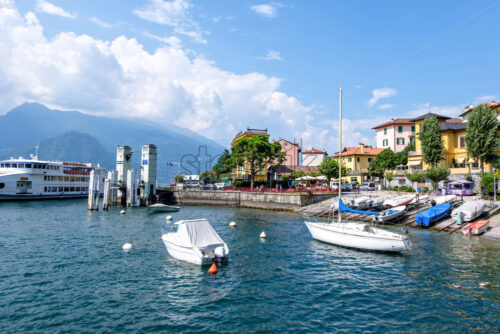 Boats and ferry parked in Varenna port. Mountains and blue sky on background. Lake Como, Italy - Starpik