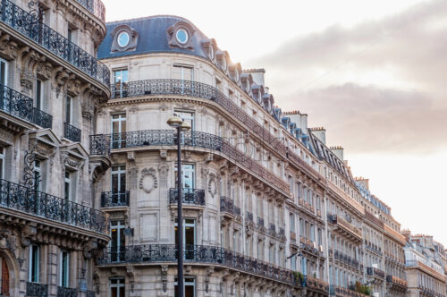 Bright sunlight bounces from beautiful ancient looking block of flats in the center of Paris. Orange and teal France. Shot at sunset. Grey sky - Starpik