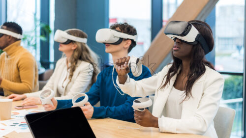 Business conference in VR in an office. Multiracial group of people using VR glasses and controllers, papers and gadgets on the table - Starpik