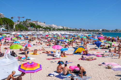 CANNES, FRANCE – AUGUST 12, 2018: Beach shore with colorful umbrellas and a lot of people. Blue sky on background - Starpik