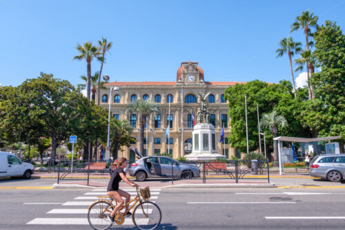 CANNES, FRANCE – AUGUST 12, 2018: The Hotel De Ville from street view. Woman riding bicycle. Blue sky on background - Starpik