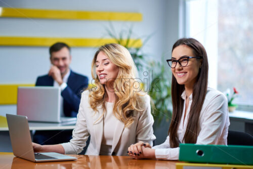 Caucasian mature women ladies at meeting table discussing a business plan with laptop computer in office. Workers on background - Starpik