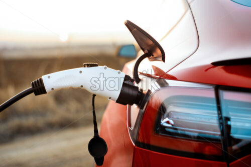 Close view of a plugged charging cable into a parked red car - Starpik