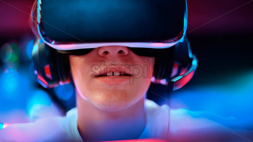 Close view of a teen playing a game console in VR headset and headphones. Blue and red illumination - Starpik