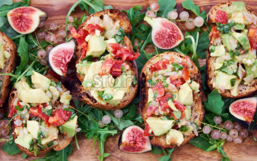 Crispy bruschetta with tomatoes, avocados and basil. Wooden plate ornated with fruits. View from top - Starpik