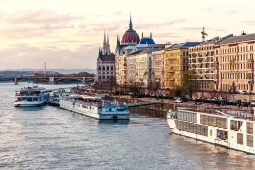 Cruise ships at sunset on Danube river. Warm sky reflecting on water. Famous parliament and city on background. Budapest, Hungary - Starpik