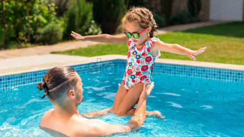 Dad holding his happy daughter in his hands in the pool - Starpik