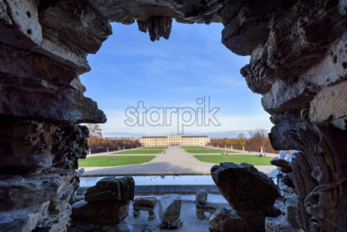 Dark view from old ancient rocks to Schonbrunn Palace gardens with tourists in bright clear day - Starpik