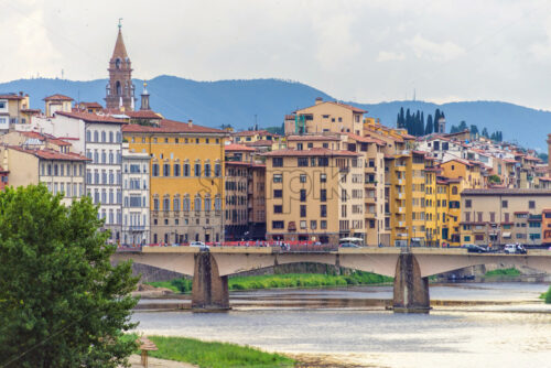 Daylight cloudy day view to bridge above Arno river with people walking and cars riding on. Buildings and trees on background, Florence, Italy - Starpik