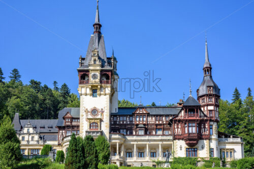 Daylight front view to ornamented facade of Peles castle with tower and bright blue sky with clouds. Romanian kings summer residence in Carpathian Mountains. Sinaia, Romania - Starpik