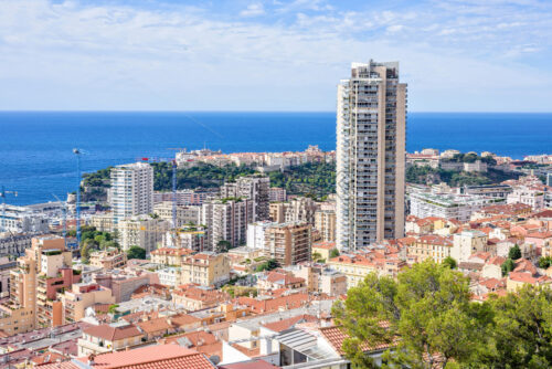 Daylight sunny view to old town, tall city hotel building and modern houses. Construction cranes working. Bright blue sky with clouds. Negative copy space, place for text. Monte Carlo, Monaco - Starpik