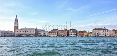 Daylight view from boat to Riva degli Schiavoni waterfront and colorful tall buildings. Bright blue sky with plane traces and clouds. Negative copy space, place for text. Venice, Italy - Starpik