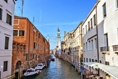 Daylight view from bridge to local canal with parked marine police boats and tall city buildings. Bright blue clear sky reflecting on water. Negative copy space, place for text. Venice, Italy - Starpik