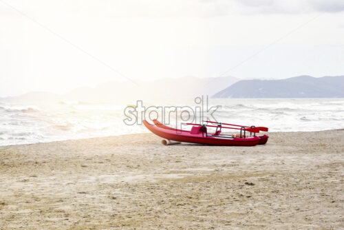 Daylight view from seaside to rising waves and mountains on background. Red boat on sand with foot traces. Bright sky with clouds. Negative copy space, place for text. Forte dei Marmi, Italy - Starpik