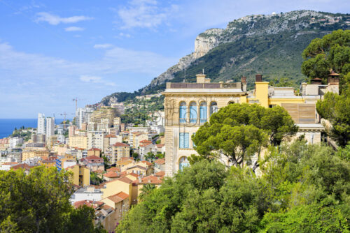 Daylight view from top to city buildings and green mountains on background. Historical architecture. Bright blue sky with clouds. Negative copy space, place for text. Monte Carlo, Monaco - Starpik