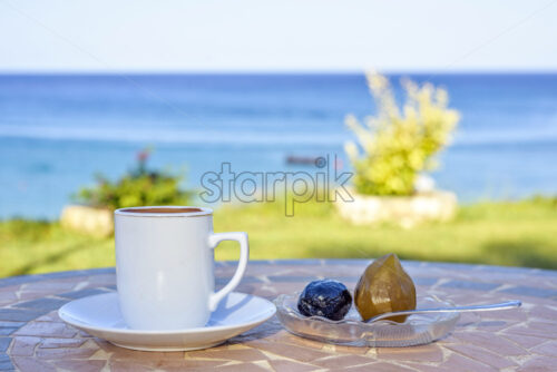 Daylight view to cup of coffee on table with local sweets and spoon. Sea view and sky on background. Protaras, Cyprus island. - Starpik