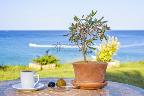 Daylight view to cup of coffee on table with local sweets, olive tree and spoon. Sea view with boat traces and sky on background. Protaras, Cyprus island - Starpik