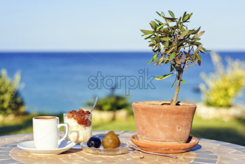 Daylight view to cup of coffee on table with local sweets, olive tree, ice cream and spoon. Sea view and sky on background. Protaras, Cyprus island - Starpik