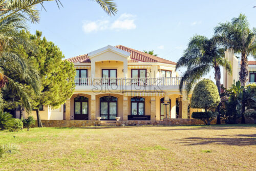 Daylight view to modern house with two levels. Green trees on side and empty garden. Bright blue clear sky. Negative copy space, place for text. Protaras, Cyprus - Starpik