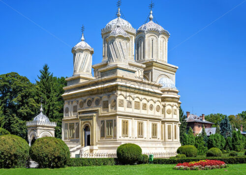 Daylight view to monastery garden park and cathedral on background. Green trees and bushes. Bright blue clear sky. Negative copy space, place for text. Curtea de Arges, Romania - Starpik