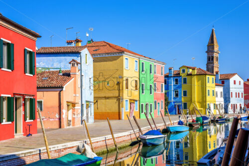 Daylight view to parked boats in a canal with image reflecting on water. Colorful buildings and bright blue clear sky. Negative copy space, place for text. Burano, Italy - Starpik