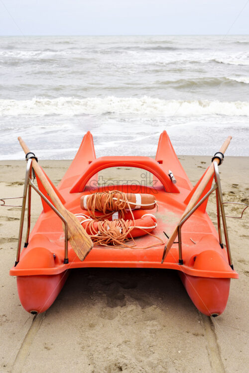 Daylight view to red boat parked on sand with two lifesavers on board. Rising waves and bright blue sky on background. Negative copy space, place for text. Forte dei Marmi, Italy - Starpik