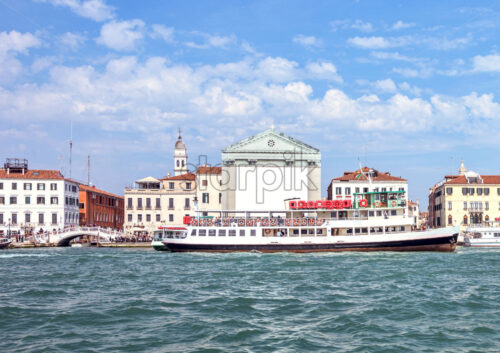 Daylight view to tourist boat cruising near Riva degli Schiavoni waterfront. Historic architecture buildings on background. Bright blue sky with clouds. Place for text. Venice, Italy - Starpik