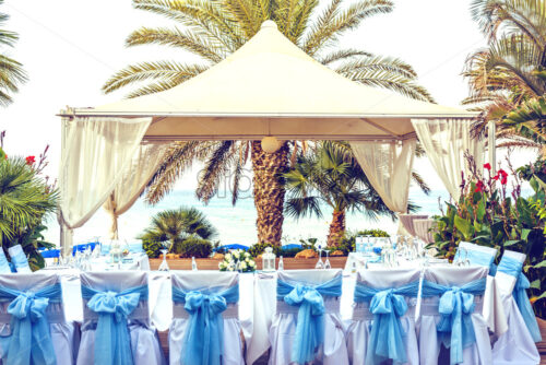 Daylight view to wedding reception table outdoors. Plates and drinks ready for serving. Plants and trees on sides. Negative copy space, place for text. Protaras, Cyprus - Starpik