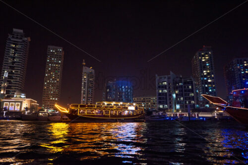 Dubai Marina at night with colorful touristic boats cruising on water. United Arab Emirates - Starpik