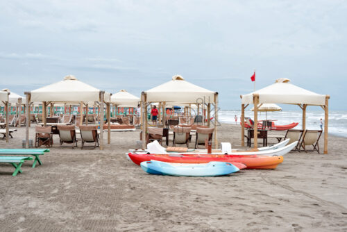 FORTE DEI MARMI, ITALY – JUNE 30, 2017: Daylight view to parked boats on sand and people talking on background. Sunchairs and sunshades. Cloudy sky. Negative copy space, place for text - Starpik