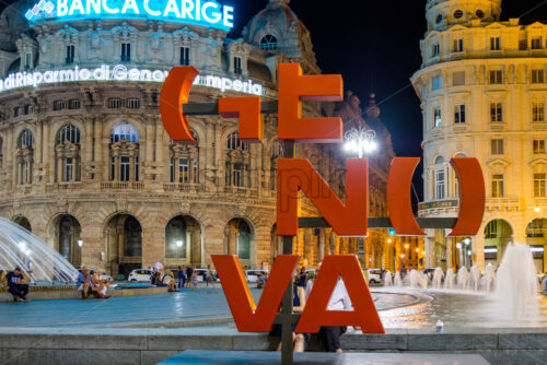 GENOA, ITALY – AUGUST 04, 2018: Piazza De Ferrari with buildings at night. Genova red sign. People on promenade having fun - Starpik