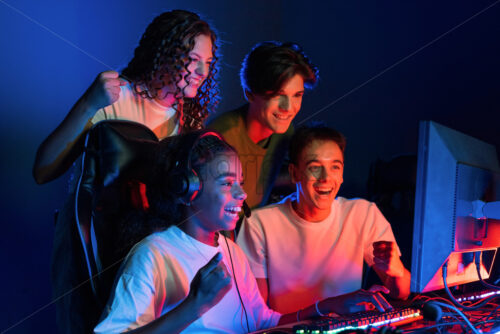 Group of multiracial teens playing video games in video game club with blue and red illumination. Excited because of a victory - Starpik