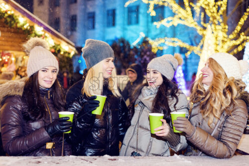 Happy smiling women friends celebrating and drinking wine at christmas market at night - Starpik