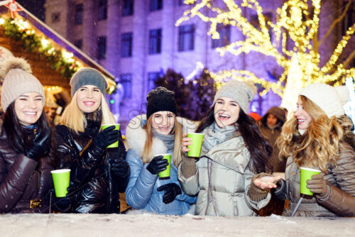 Happy smiling women friends celebrating and drinking wine at christmas market at night - Starpik