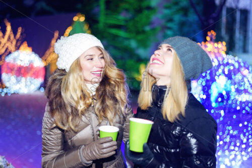 Happy smiling women friends celebrating and drinking wine at christmas market at night - Starpik