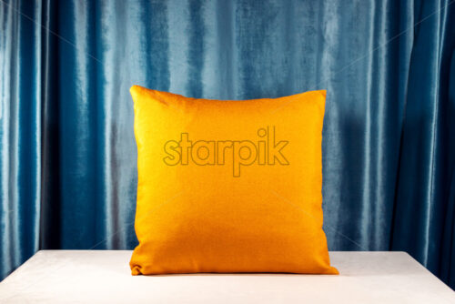 Horizontal shot of an orange pillow on the desk. Blue velvet background. Light casting soft shadows on the table. Interior design idea - Starpik